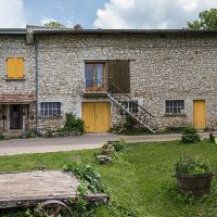 Adroite, le gîte 7-9 places avec son mur en bois cordé, au centre, l'escalier qui conduit à la salle de réunion, à gauche la maison familiale Gîte Entre Ciel et Pierres