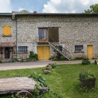 Adroite, le gîte 7-9 places avec son mur en bois cordé, au centre, l'escalier qui conduit à la salle de réunion, à gauche la maison familiale Gîte Entre Ciel et Pierres