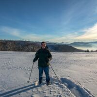 Frédéric équipé de raquettes et d'un sourire. Au loin à gauche les crêtes enneigées des hauts plateaux du Vercors Randonnée en raquettes